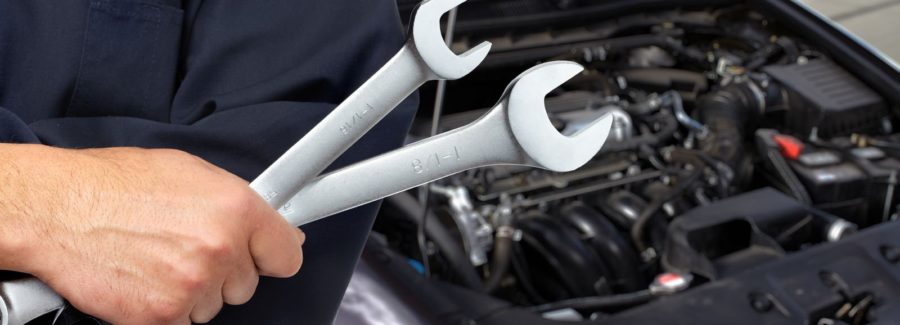 Mechanic standing in front of car with two wrenches in hand. Car repair.